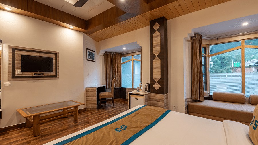 A spacious hotel room with a large bed, a TV, a desk, and a window with a view - DLS Meghavan Resort